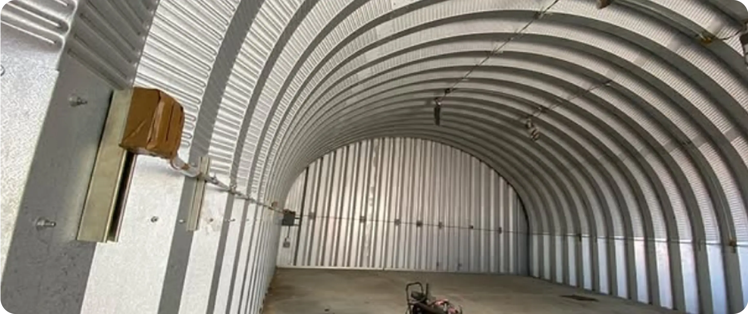 Metal Quonset hut building interior before spray foam insulation — bare corrugated walls and ceiling